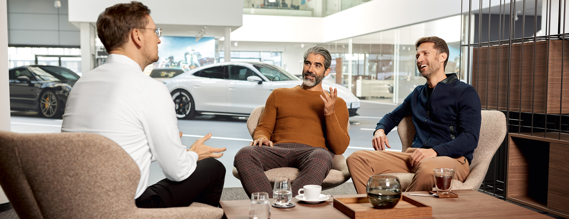 Ein Porsche Verkäufer führt ein Mitarbeitergespräch mit zwei Porsche Kunden.